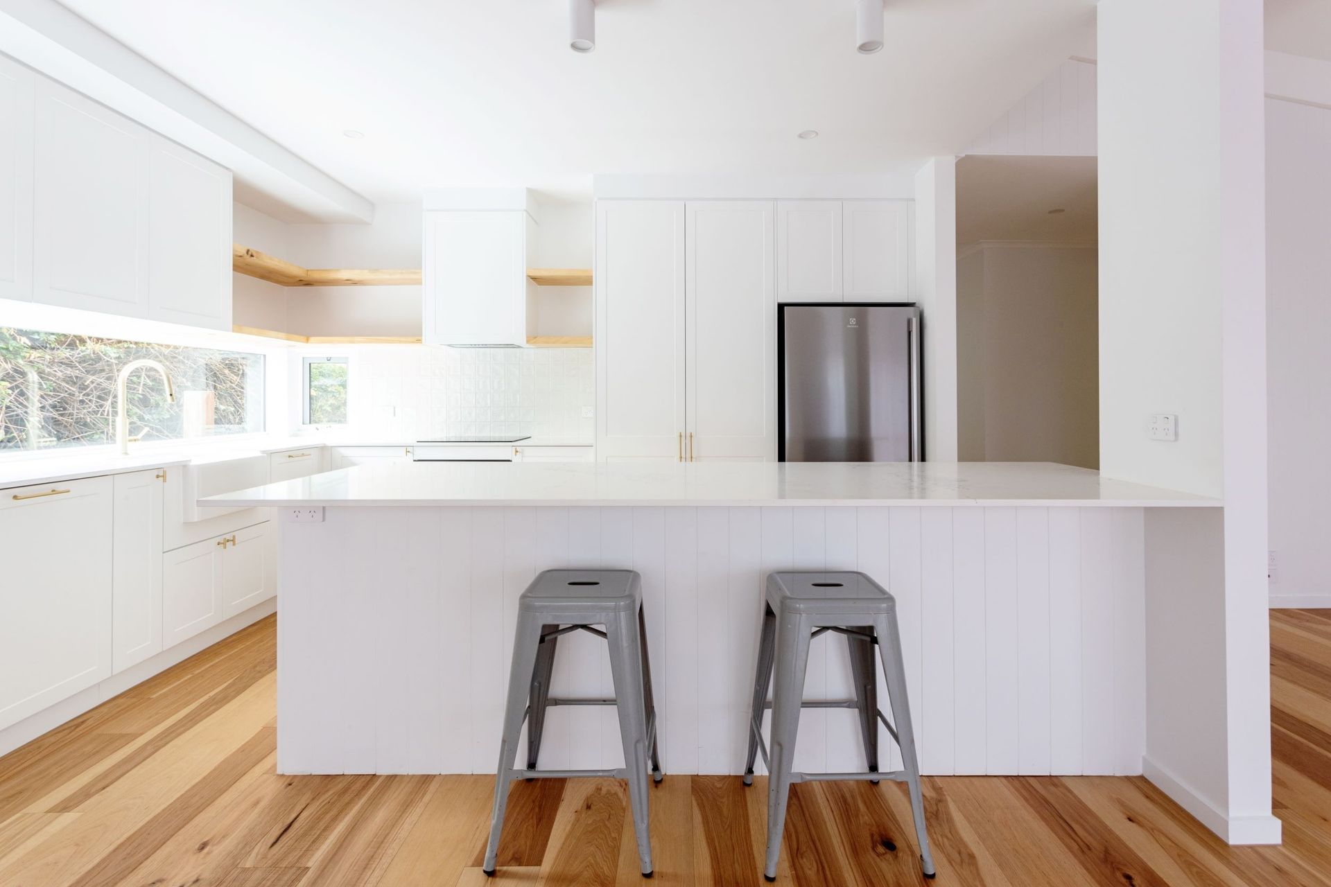 Modern white kitchen with island, stainless steel refrigerator, and two gray bar stools.
