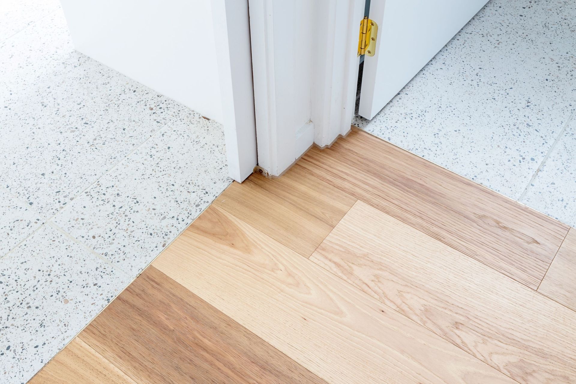 A doorway showing a transition from terrazzo flooring to wooden planks.