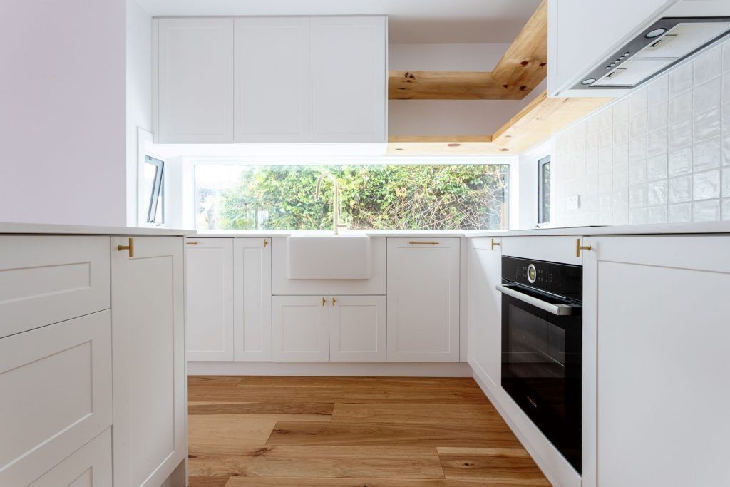 White kitchen with wooden floor, cabinets, oven, and large window overlooking greenery.