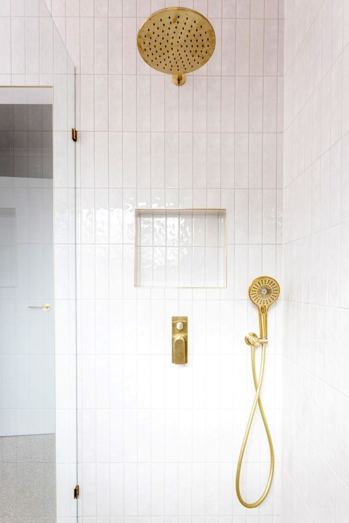 Gold shower fixtures against white tiled wall. Includes overhead shower, hand shower, and in-wall controls.