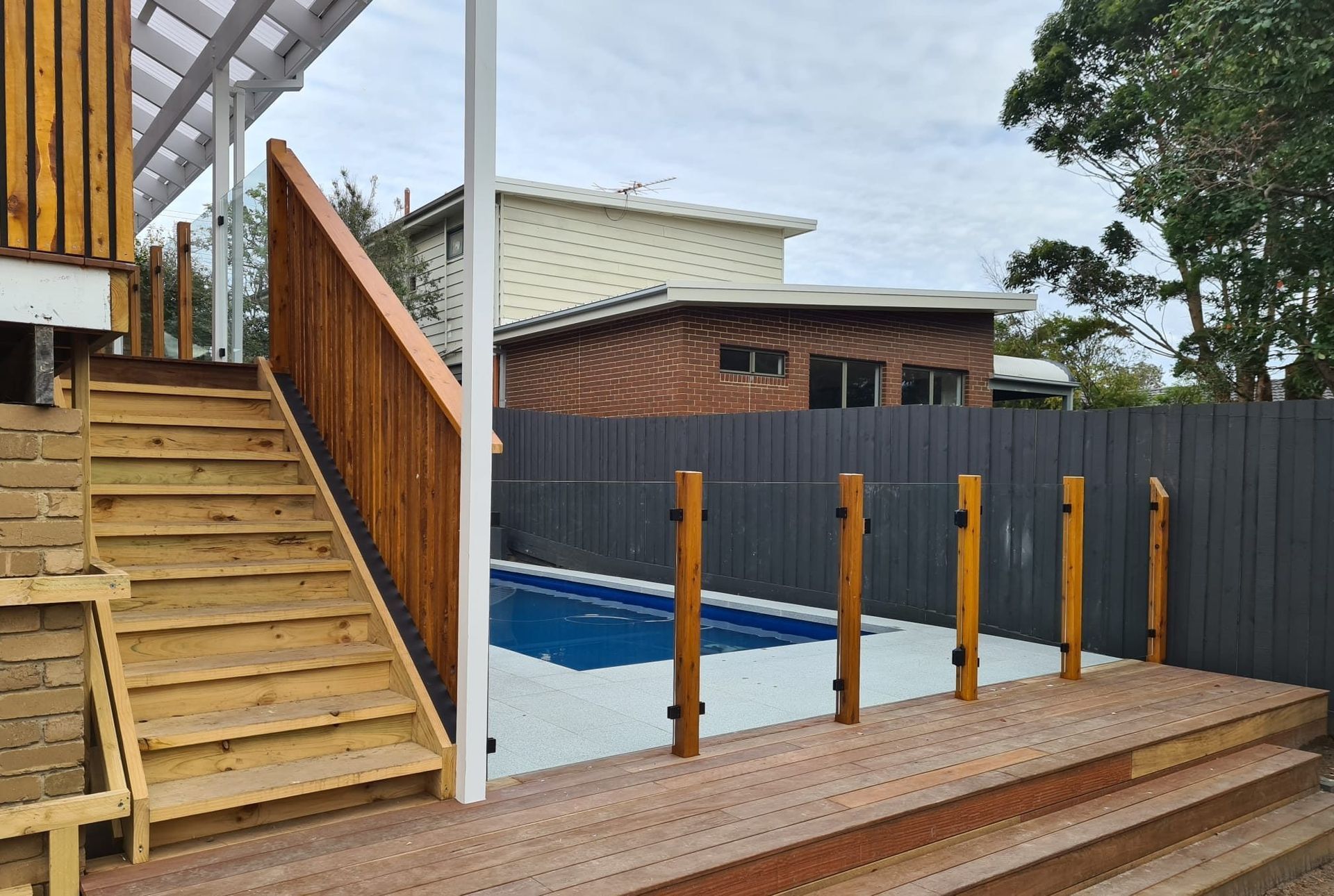 Wooden stairs and deck lead to a small pool behind a gray fence.