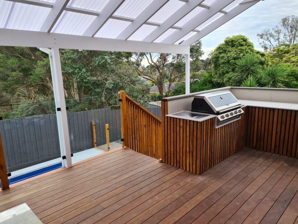 Outdoor wooden deck with built-in grill and overhead pergola.