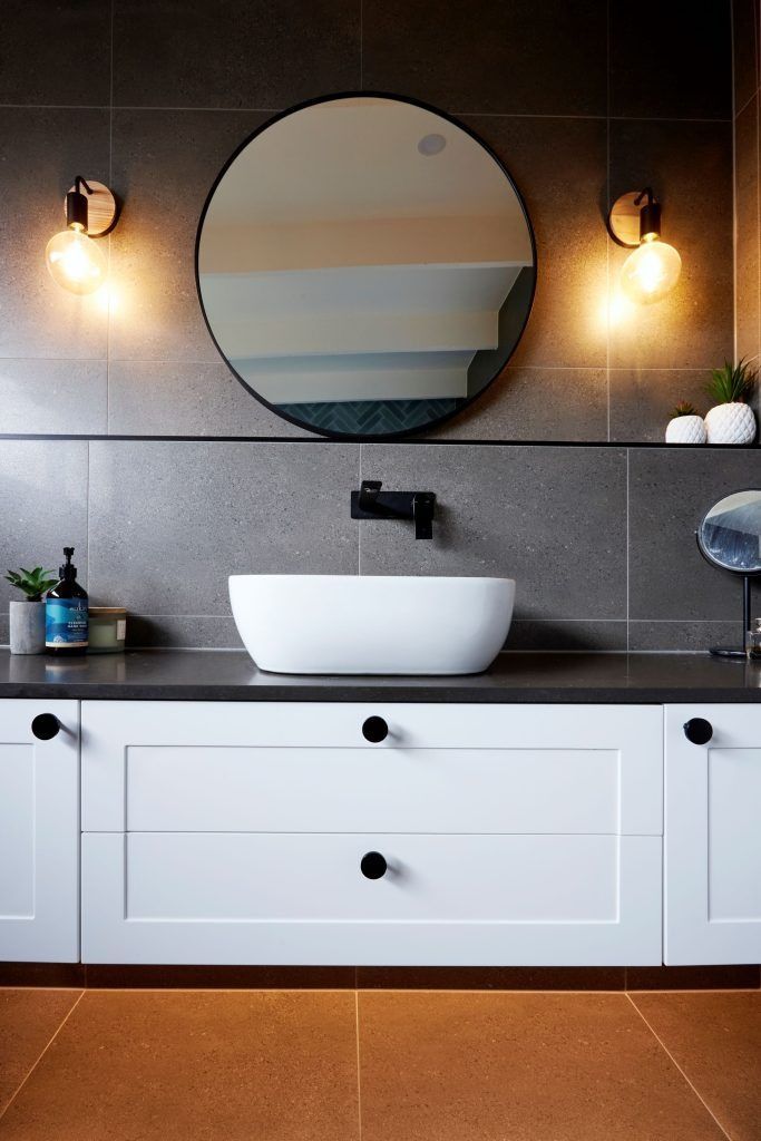 Modern bathroom with a white sink, round mirror, and black accents on gray tile.