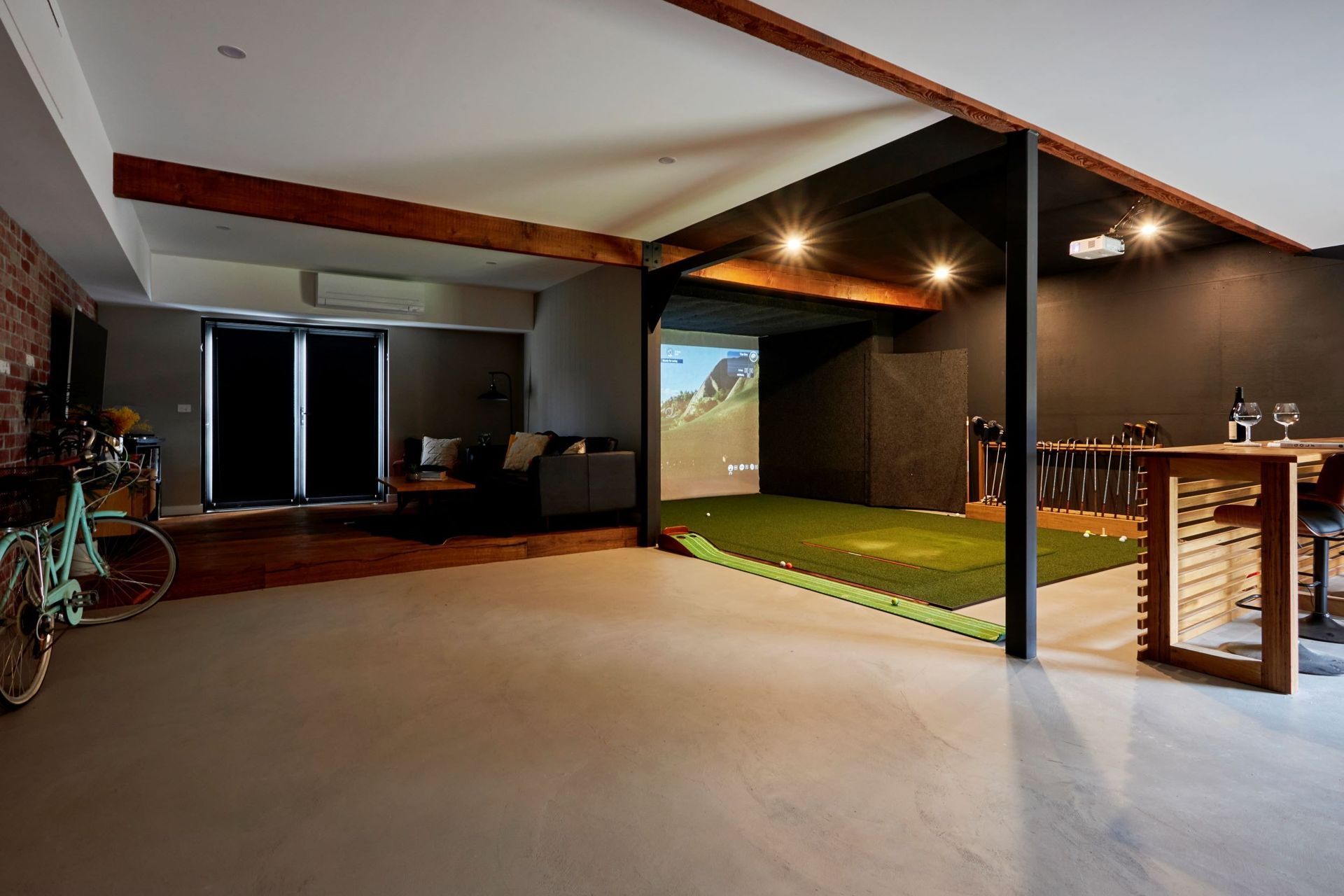 Spacious room with golf simulator, seating area, exposed brick, and a bicycle.