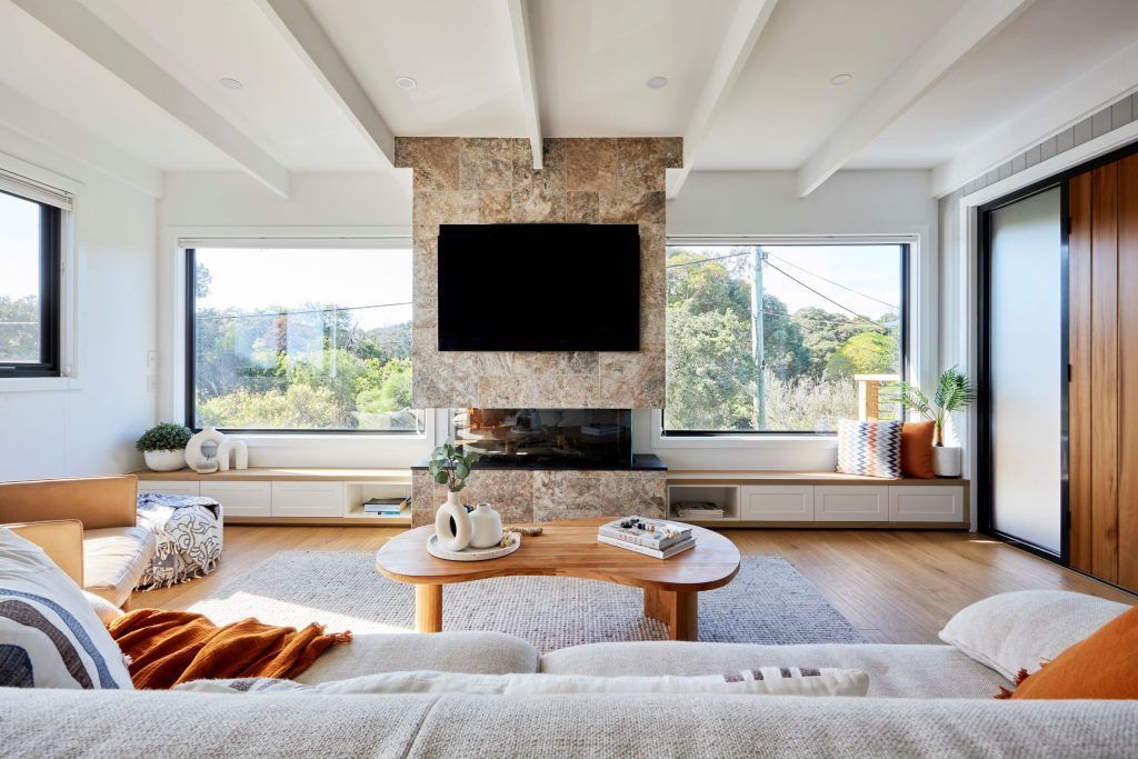 Spacious living room with fireplace, TV, large windows, and light wood floors.