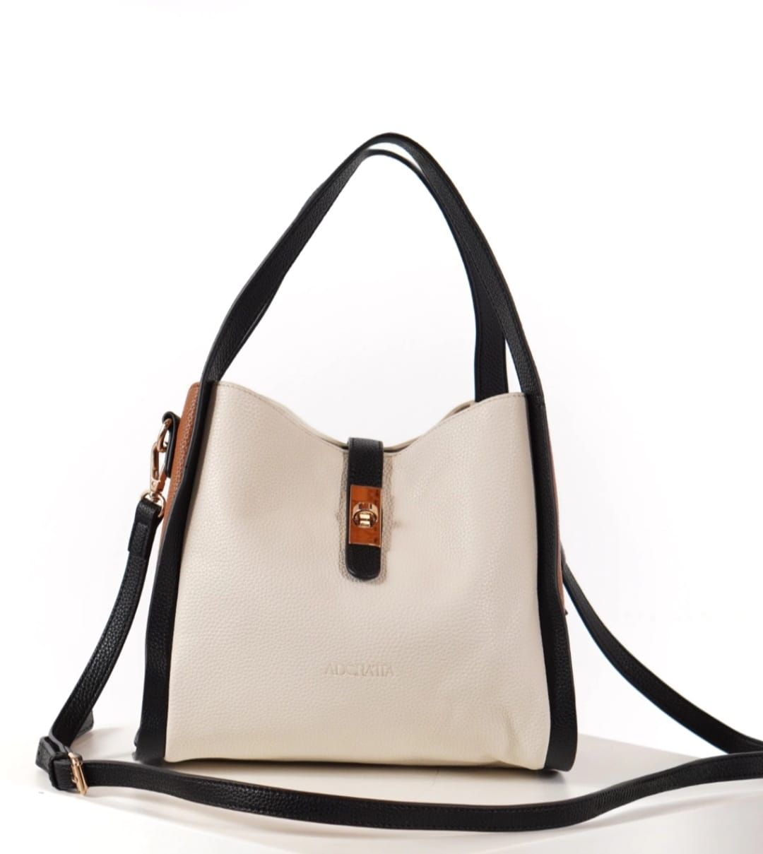 Bolso color crema con ribete, asas y correa en negro. Tiene cierre de hebilla y reposa sobre una superficie blanca.