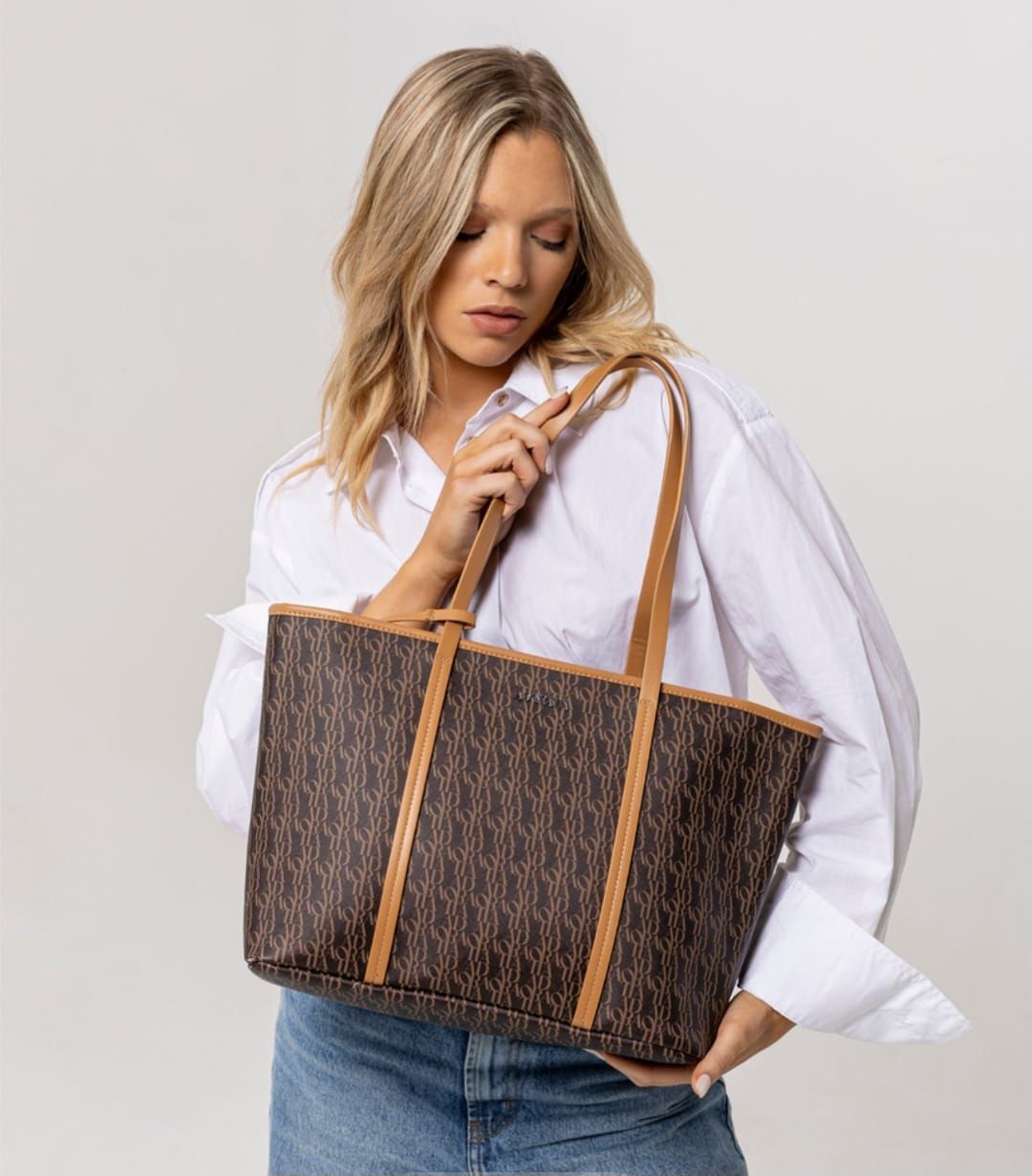 Bolso de mano marrón con bolsa pequeña a juego; ambos con patrón repetido y asas y ribetes en color tostado.