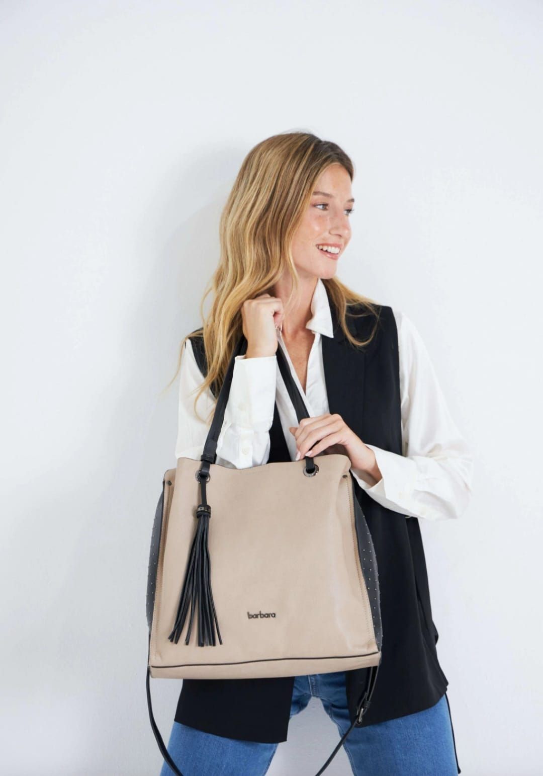 Bolso de mano de color beige con asas y borla de color azul oscuro, lleva adjunta una correa para el hombro.