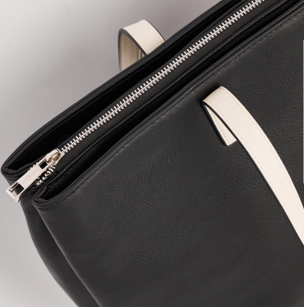 Bolso tote de color negro con correas en color crema, sobre fondo blanco.