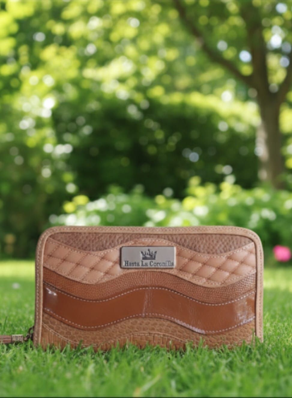 Cartera de cuero marrón y tostado sobre césped verde con fondo borroso de árboles.