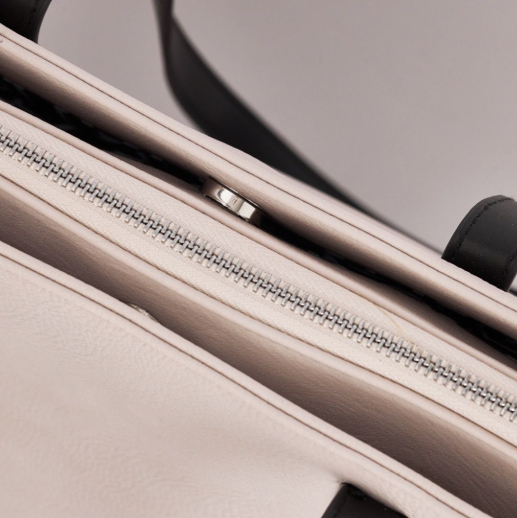 Bolso de mano de color rosa con tiras negras sobre fondo blanco.