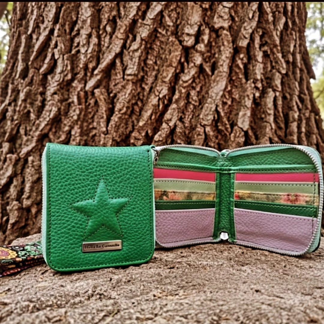 Cartera de piel verde con estrella y correa de muñeca floral; cartera abierta que muestra ranuras para tarjetas.