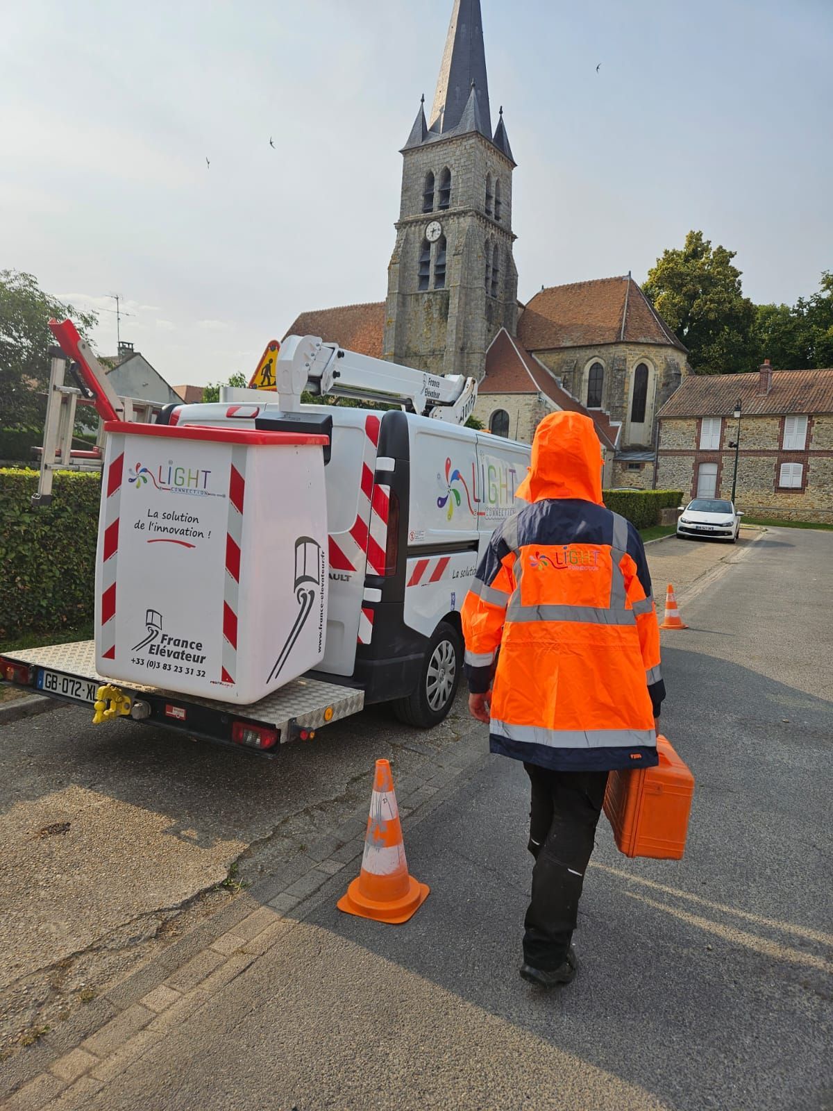 Un homme vêtu d'une veste orange se dirige vers une camionnette blanche.