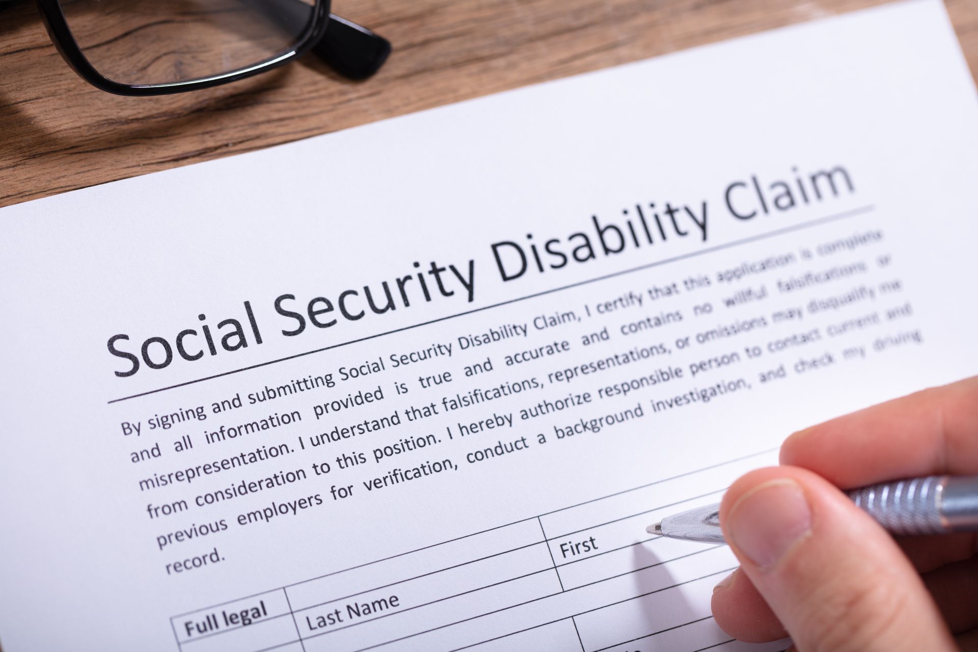 Person signing a Social Security Disability Claim form. Glasses are visible.