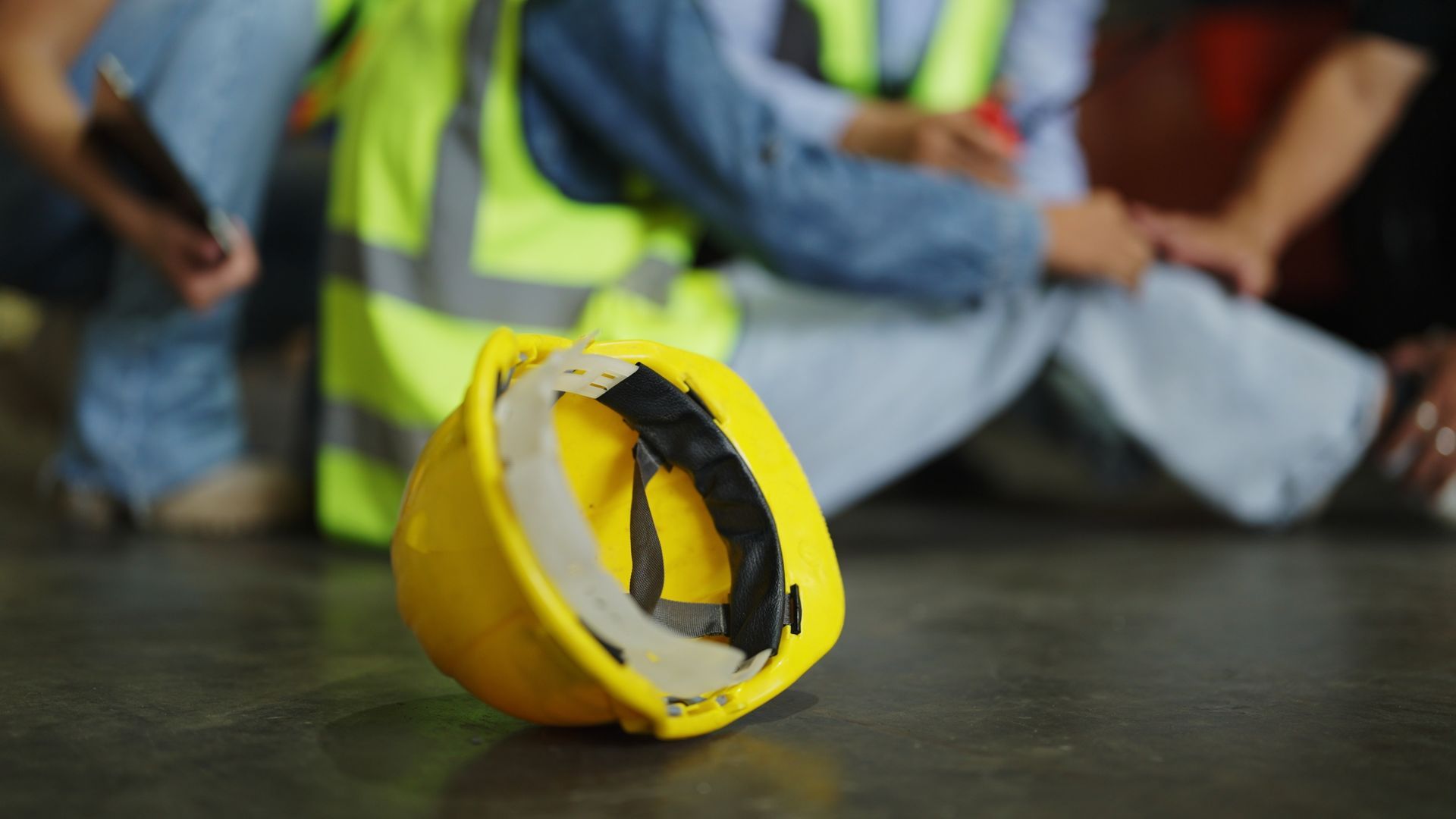 Yellow hard hat on floor near people in safety vests after an accident.
