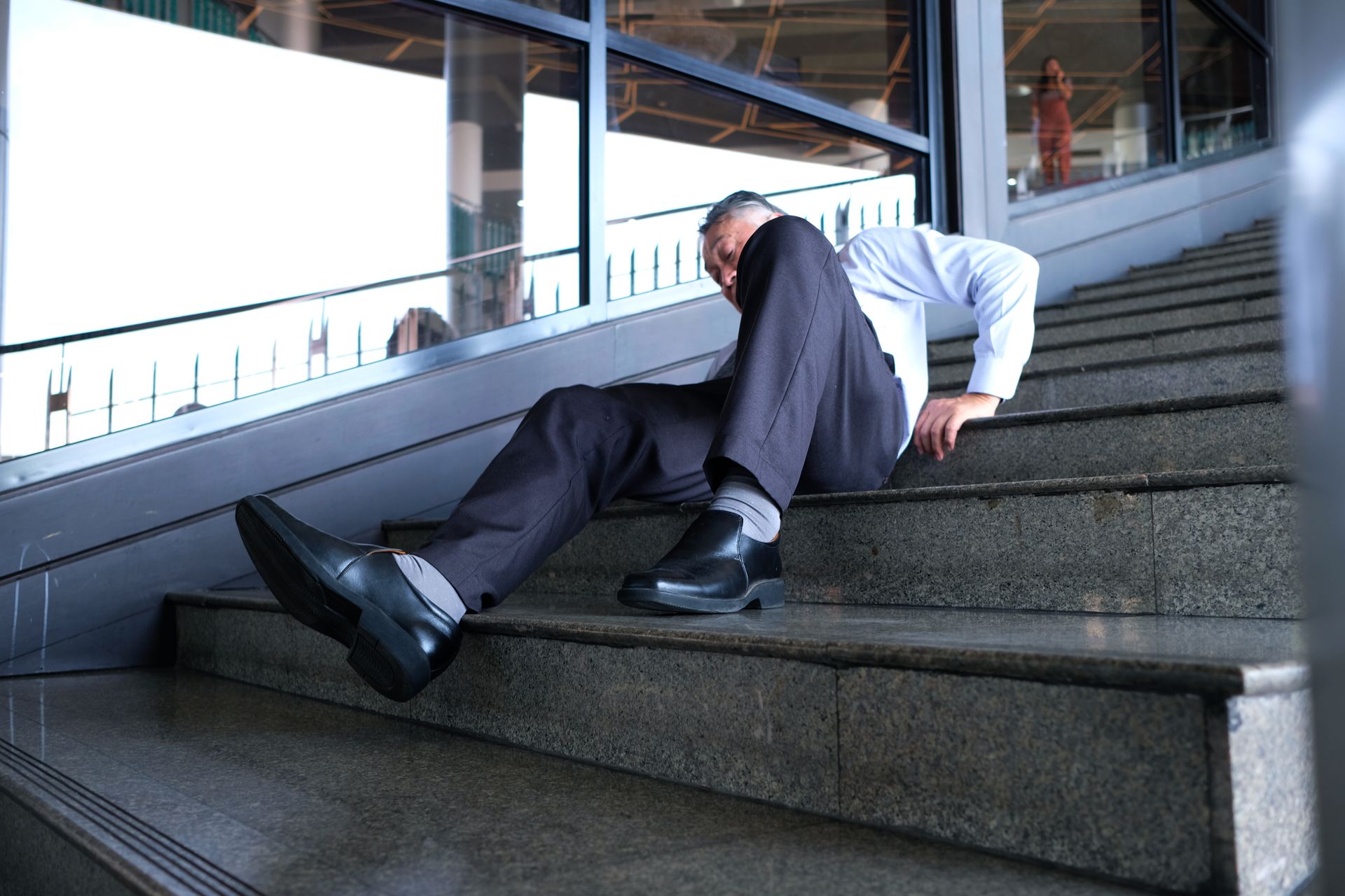 Man in a suit lying on stairs, appearing to have fallen in a building interior.