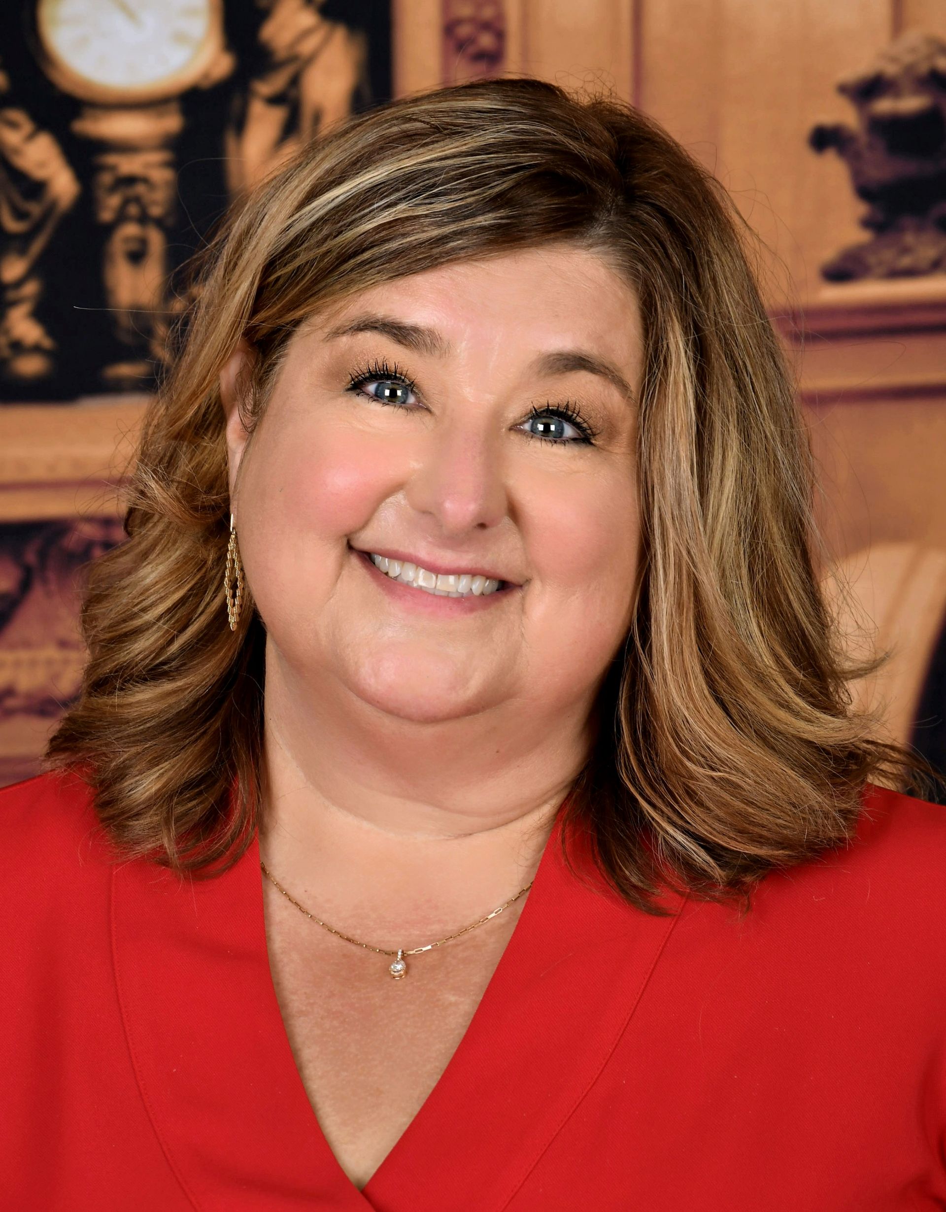 A woman in a red shirt is smiling in front of a clock.