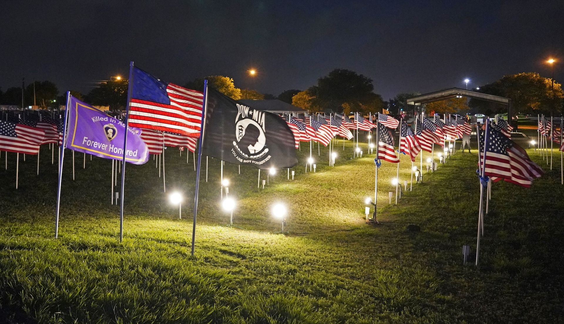 A field of american flags are lit up at night