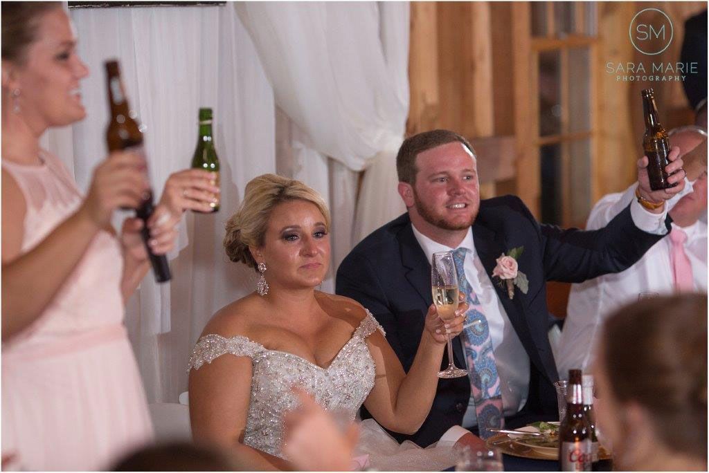 A Bride and Groom Are Sitting at A Table with Their Wedding Party Holding Beer Bottles - Lee’s Summit, MO - Top Shelf Bartending Services, LLC