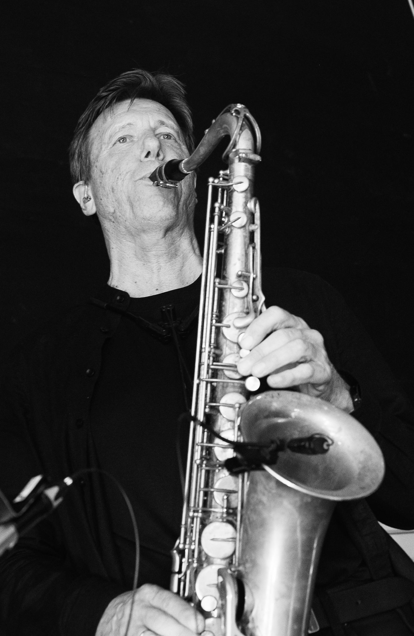 Man playing saxophone, lit from below, in black and white.