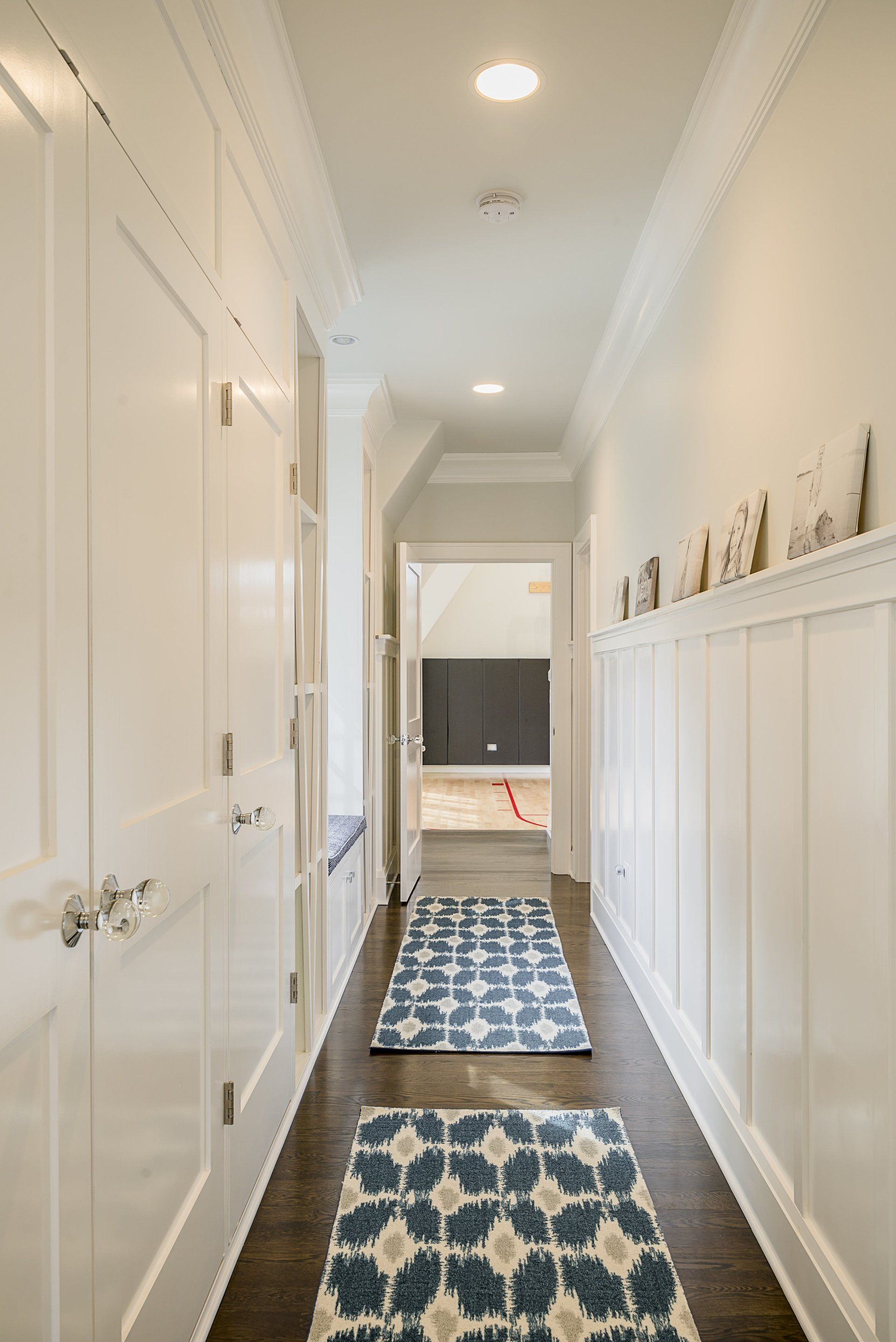 A long hallway with a blue and white rug on the floor leading to a bedroom.