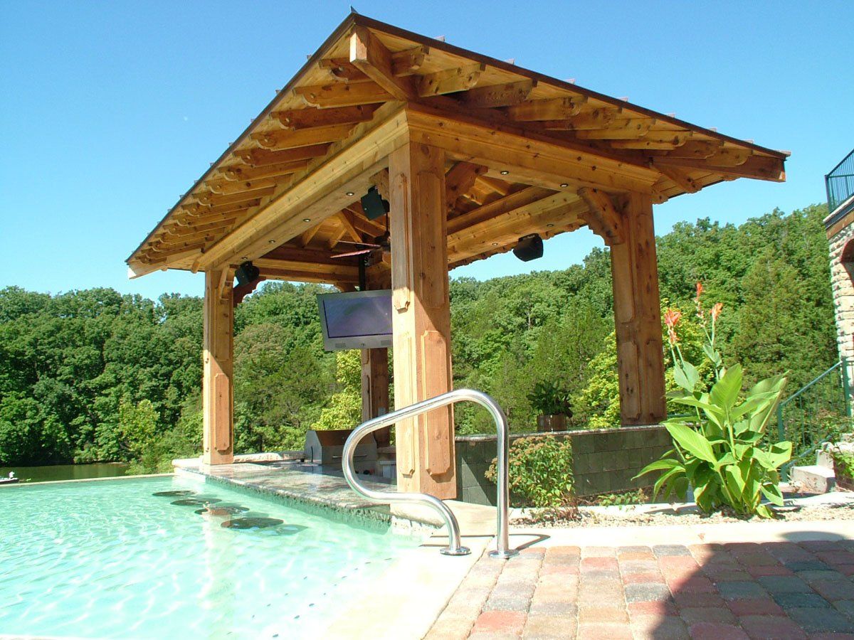 A wooden gazebo over a swimming pool with trees in the background