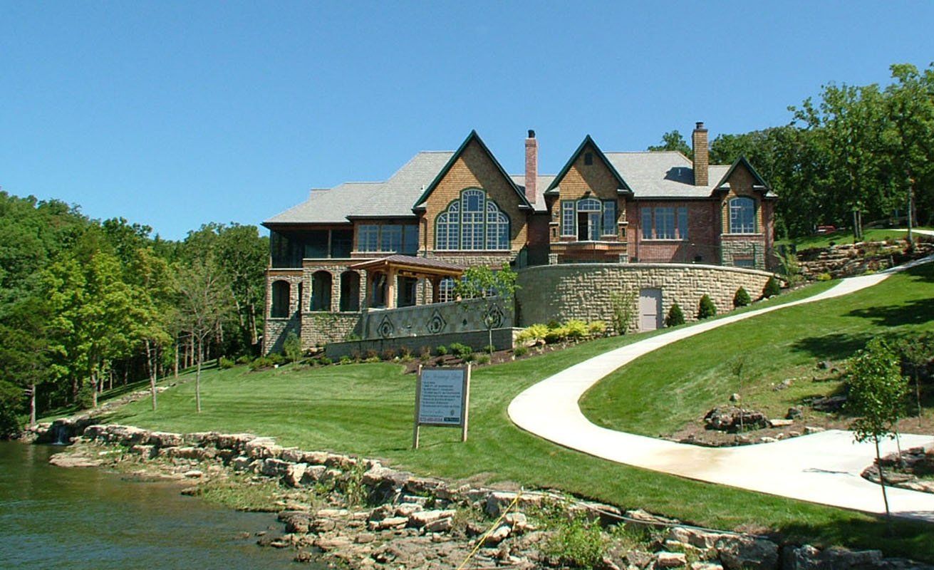A large house sits on a hill next to a lake