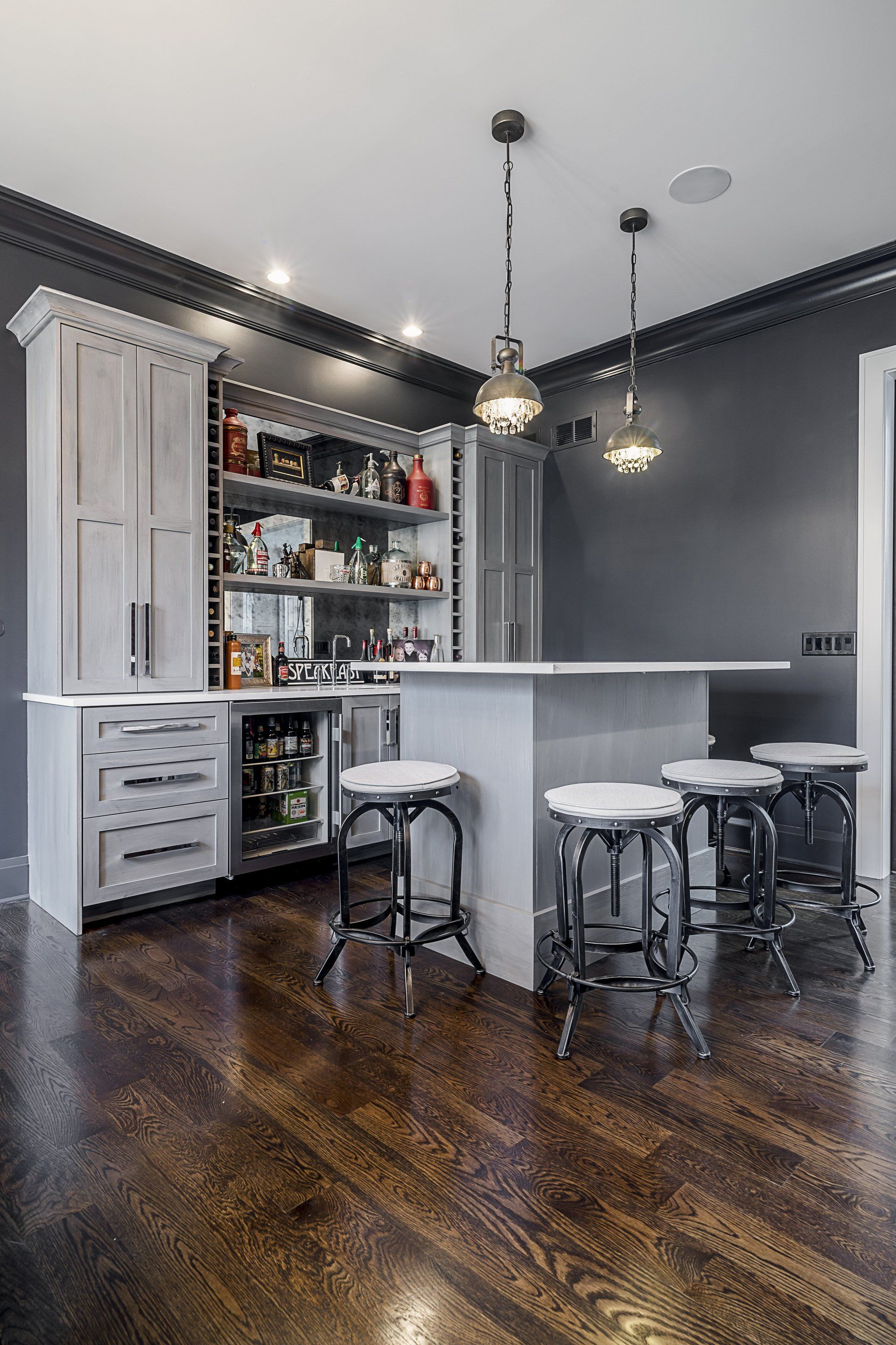 A kitchen with a large island and stools and a wine cooler.