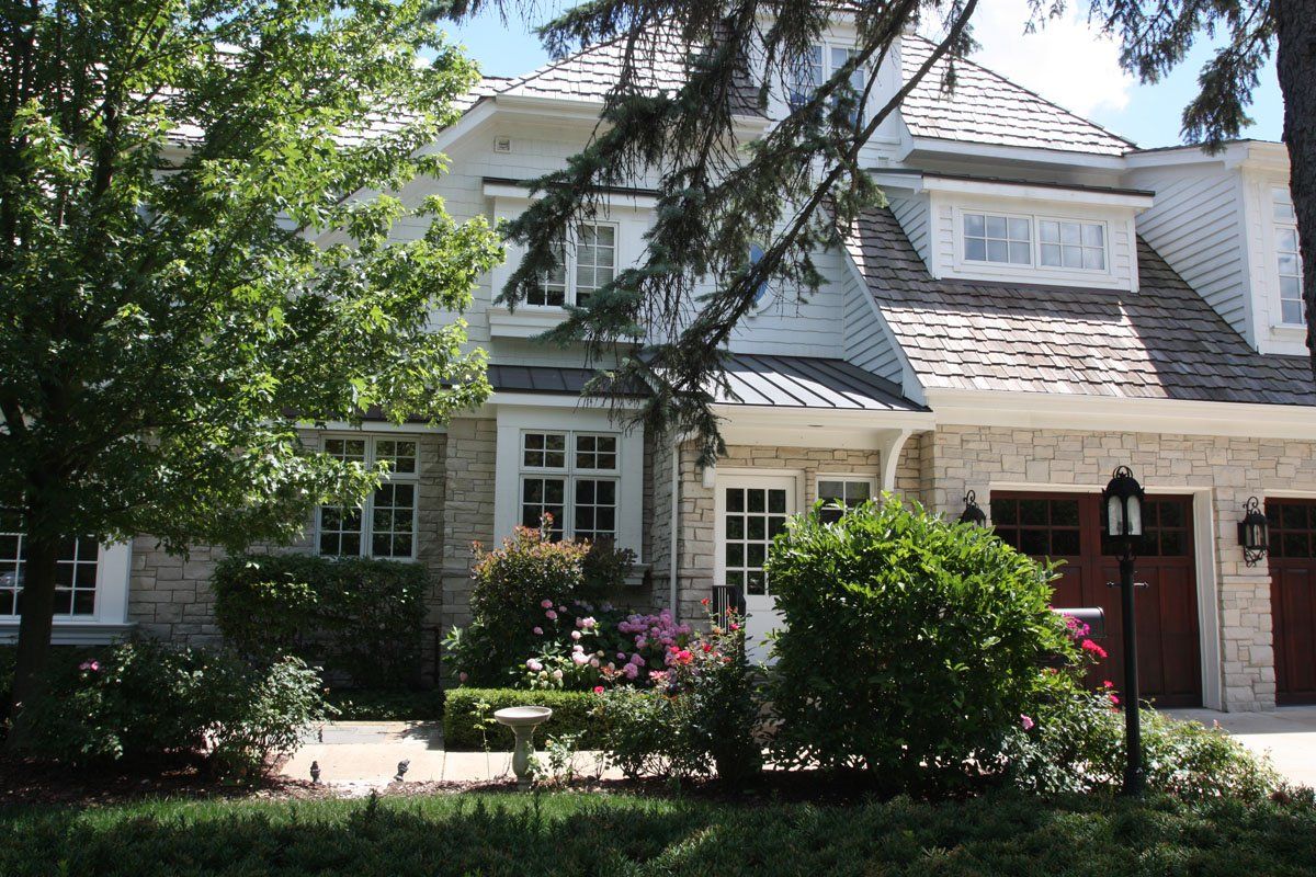 A large house with a red garage door is surrounded by trees and bushes