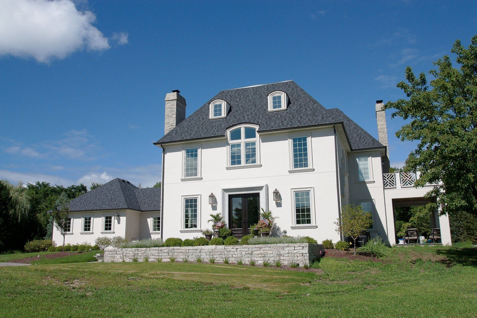 A large white house with a gray roof is sitting on top of a lush green field.