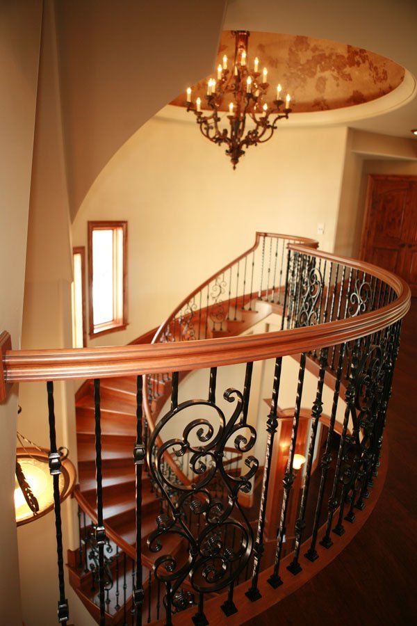 A spiral staircase with a wrought iron railing and a chandelier hanging from the ceiling