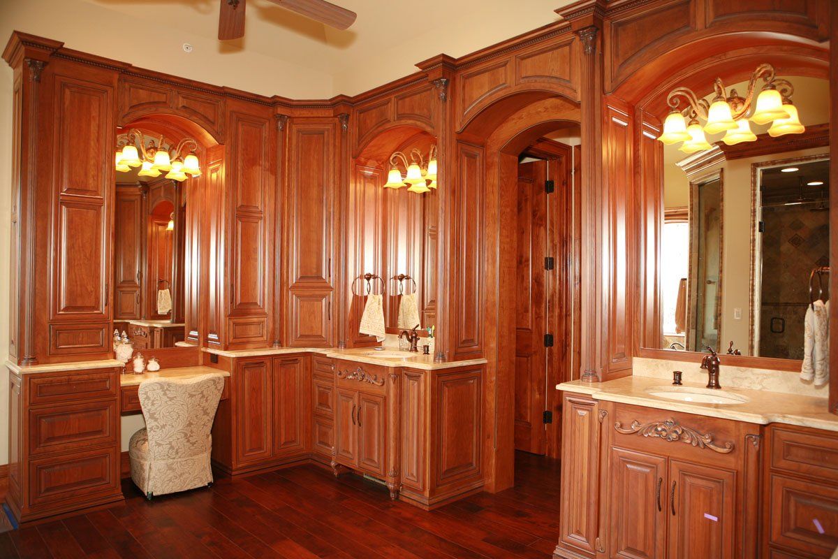 A bathroom with wooden cabinets , sinks , mirrors and a ceiling fan.