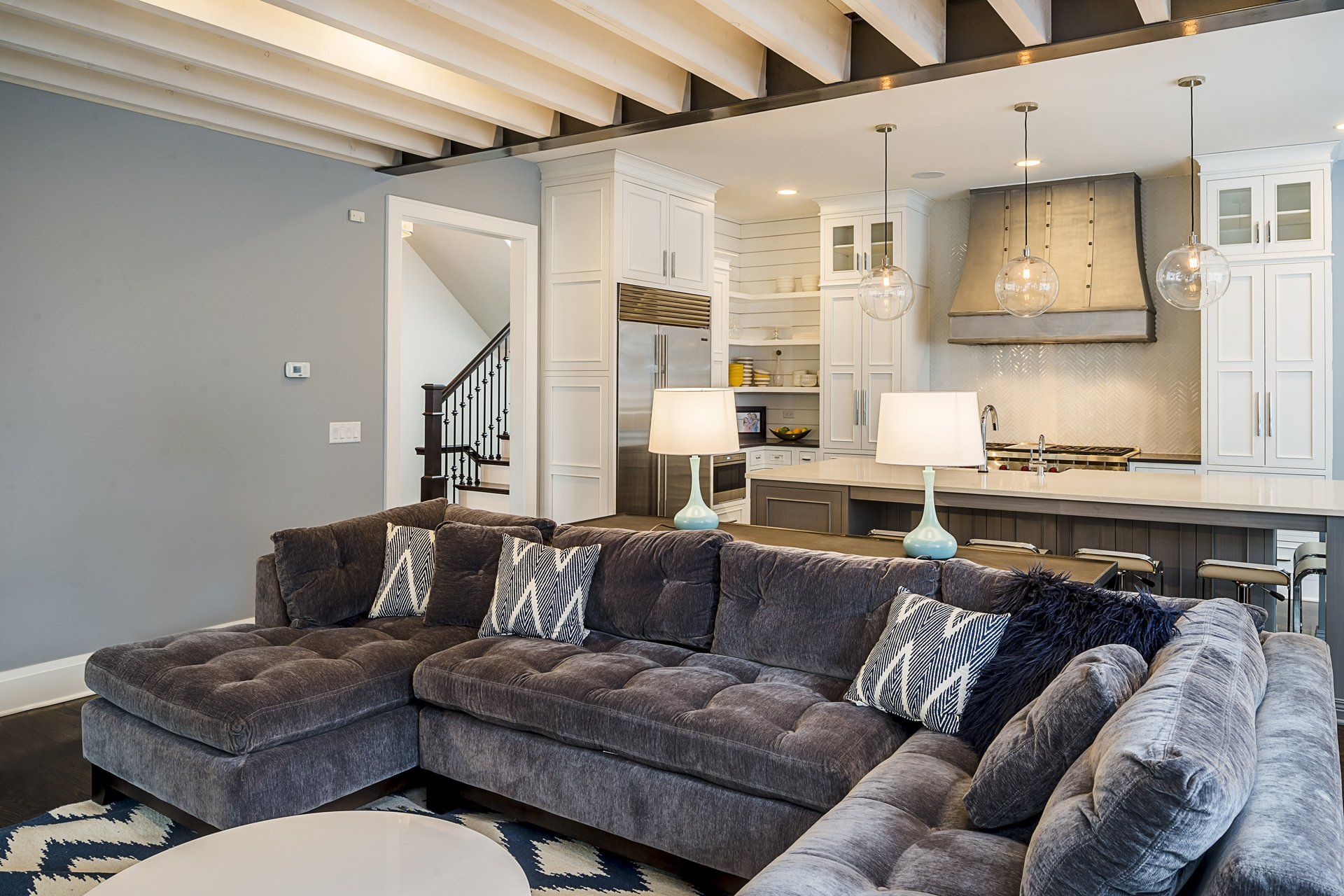 A living room with a large sectional couch and a kitchen in the background.