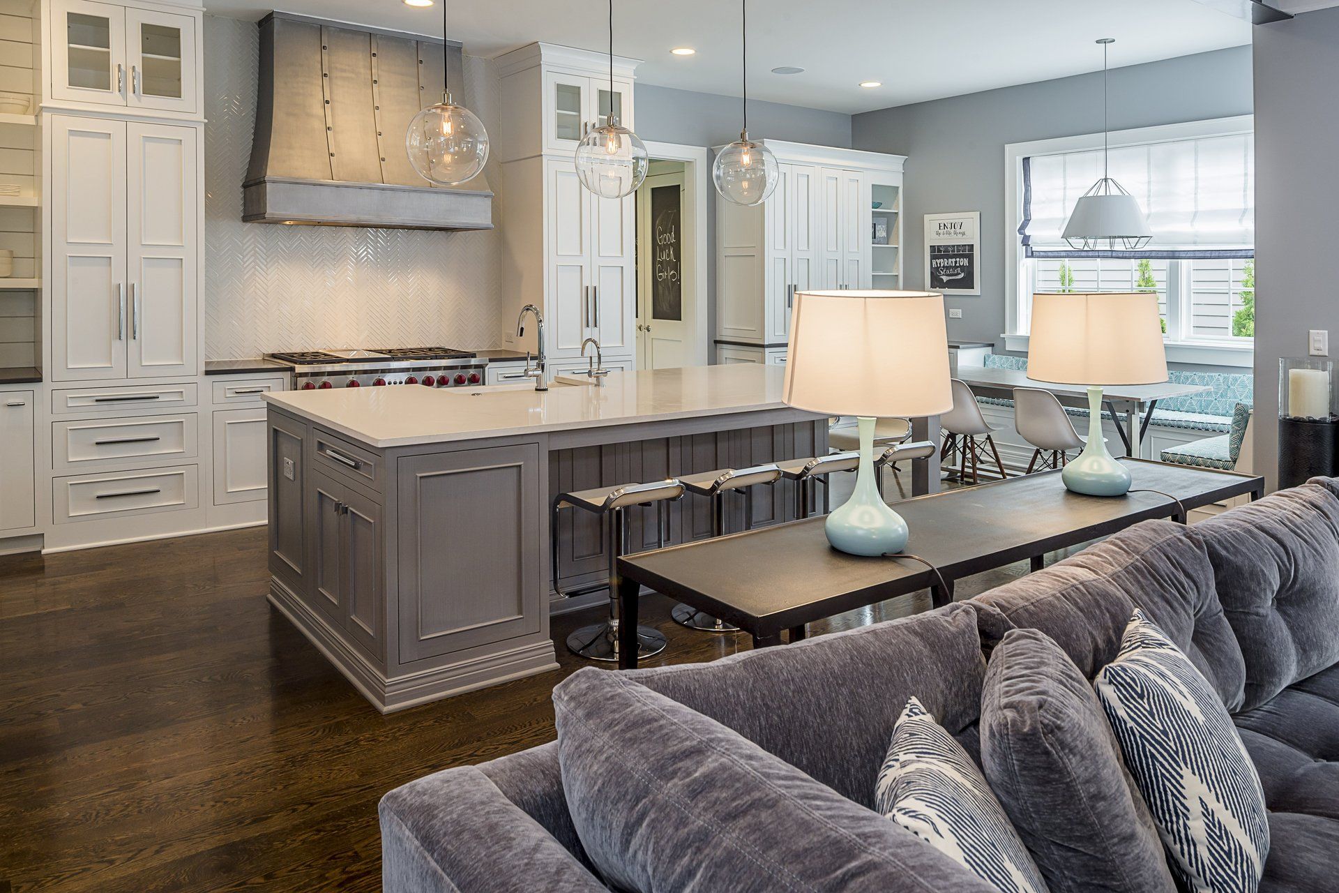 A living room with a couch , table , lamps and a kitchen.