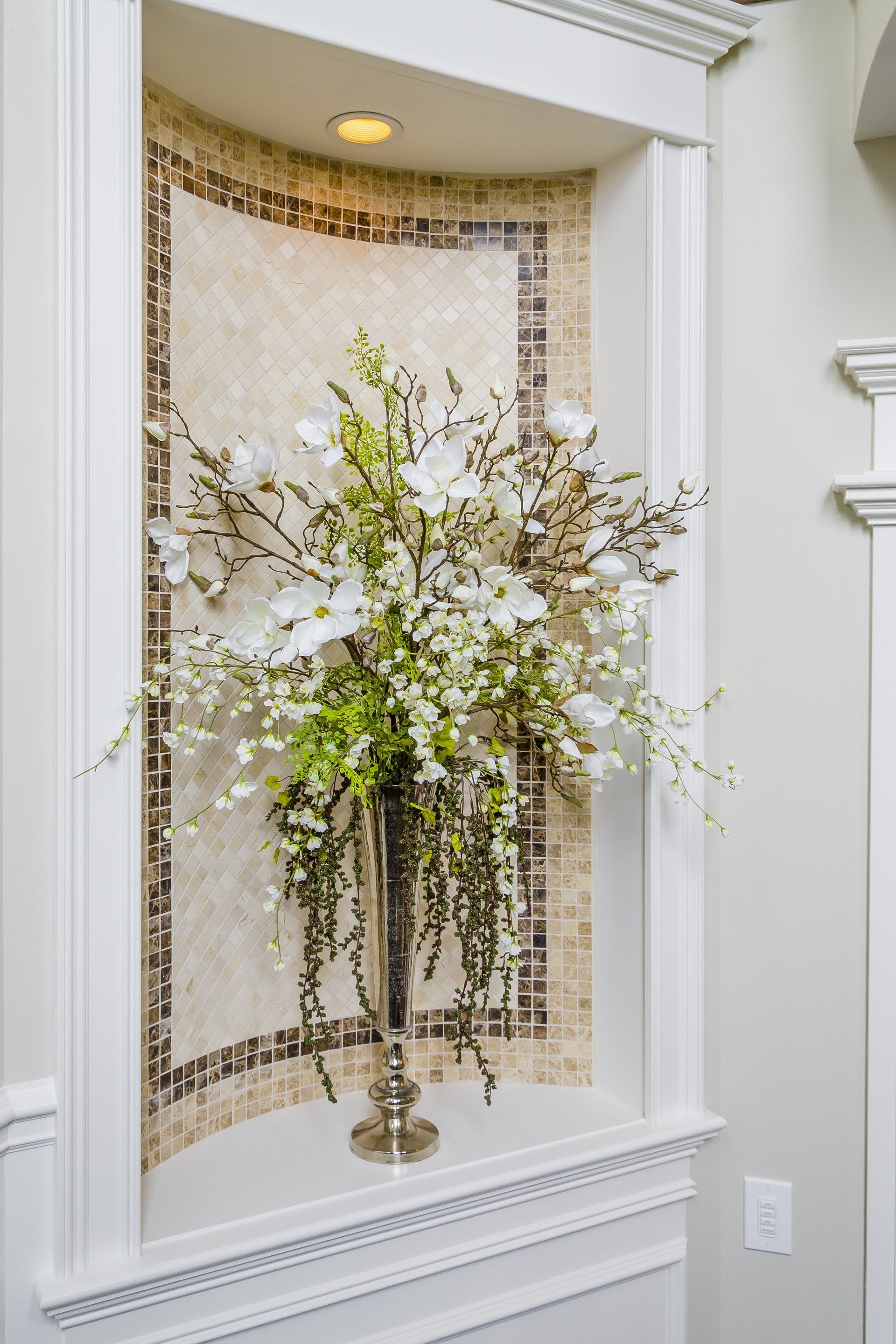 A vase filled with flowers is sitting in a niche on a wall.
