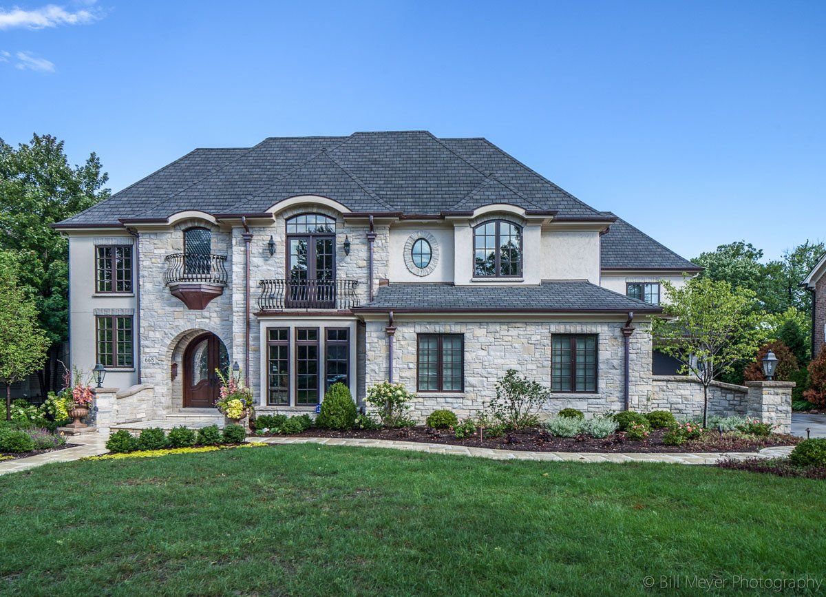 A large white house with a gray roof is sitting on top of a lush green lawn.