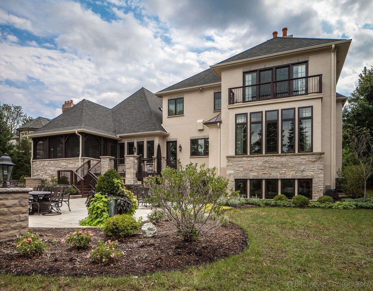 A large house with a lot of windows is sitting on top of a lush green field.