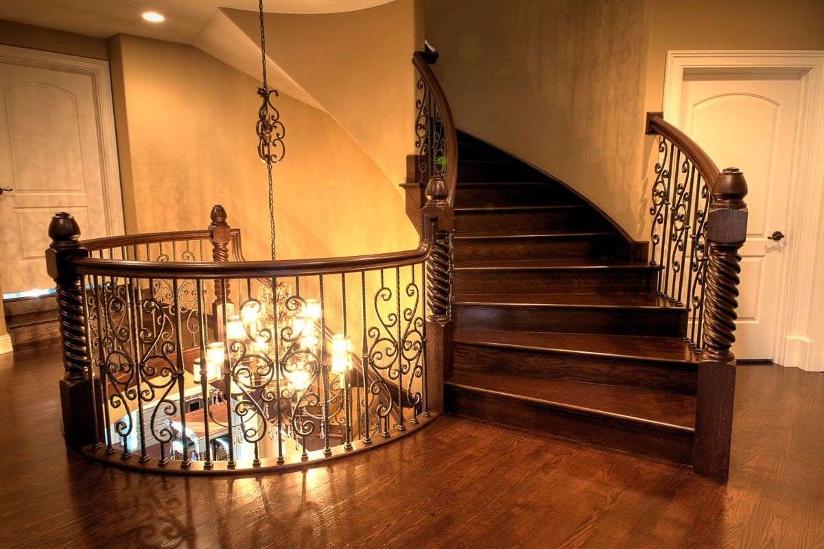 A spiral staircase with a wrought iron railing and a chandelier hanging from the ceiling