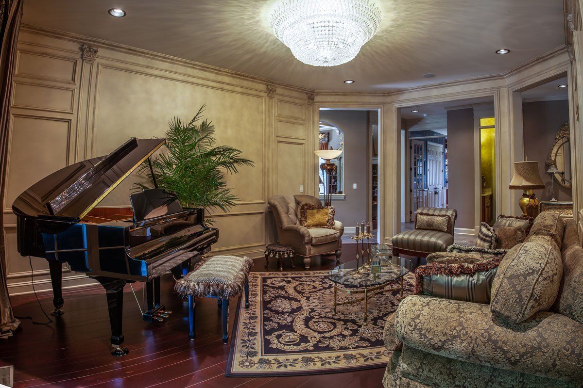A living room with a piano , chairs , and a chandelier.