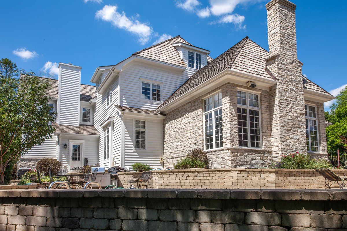 A large white house with a stone chimney and a brick wall in front of it.