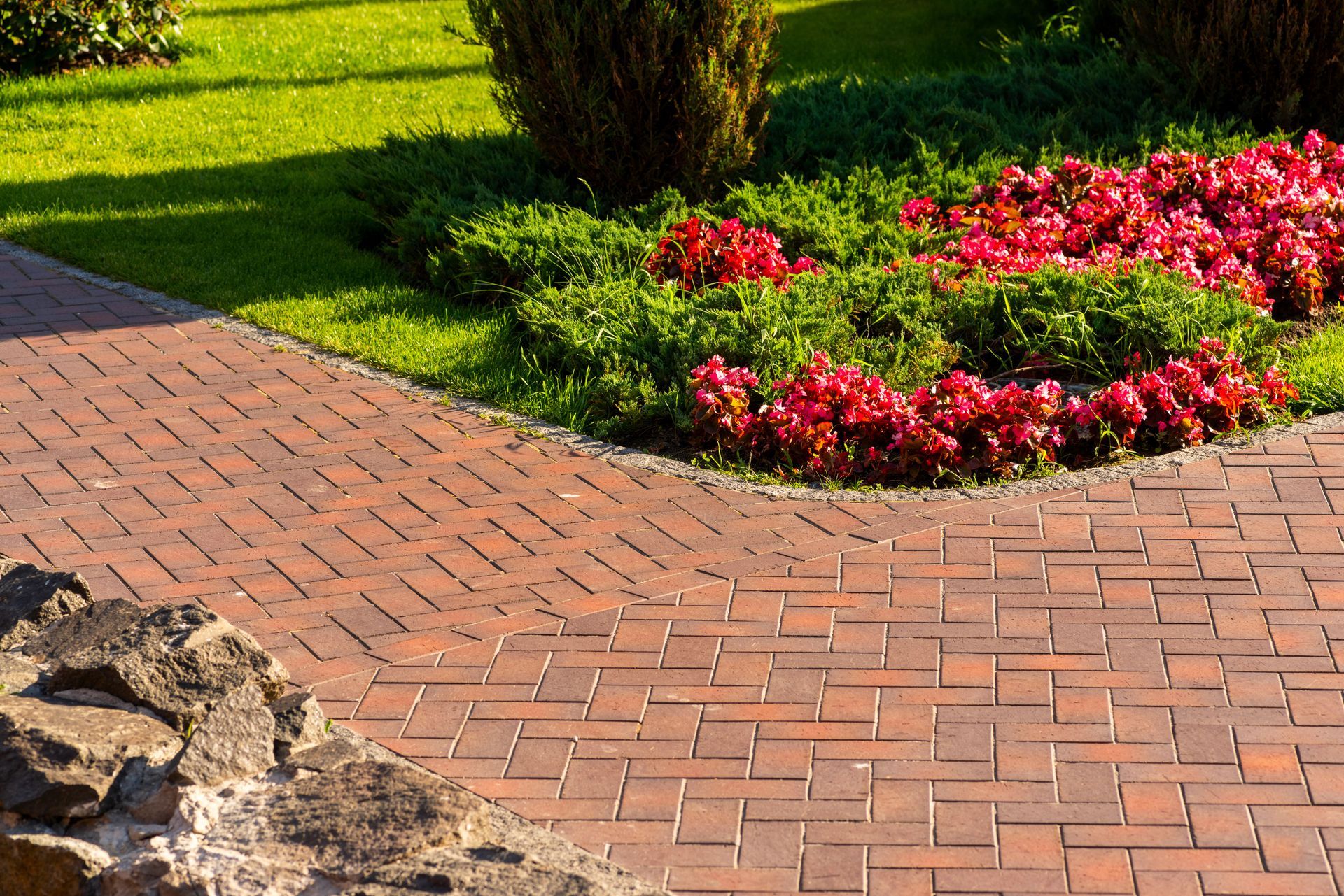 Pathway made of red paving slabs running alongside a vibrant array of flowers in a beautifully designed landscape.