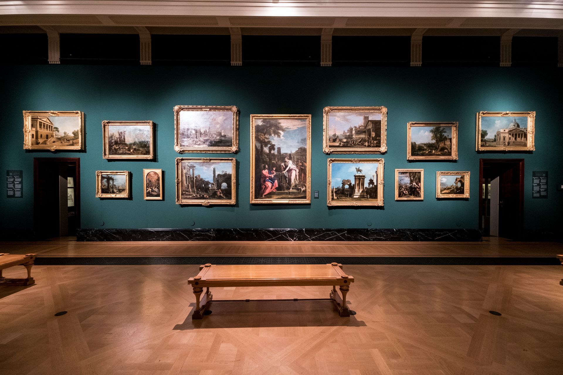 Art gallery with a bench and green walls with several paintings with gold frames