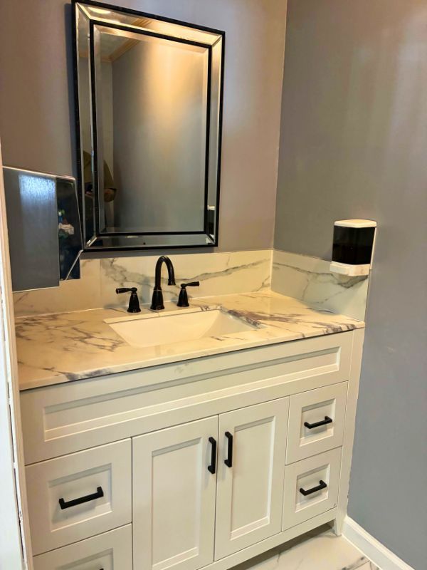 Remodeled bathroom with marble countertop, white vanity, black fixtures, and framed mirror by Eli’s Roofing LLC.