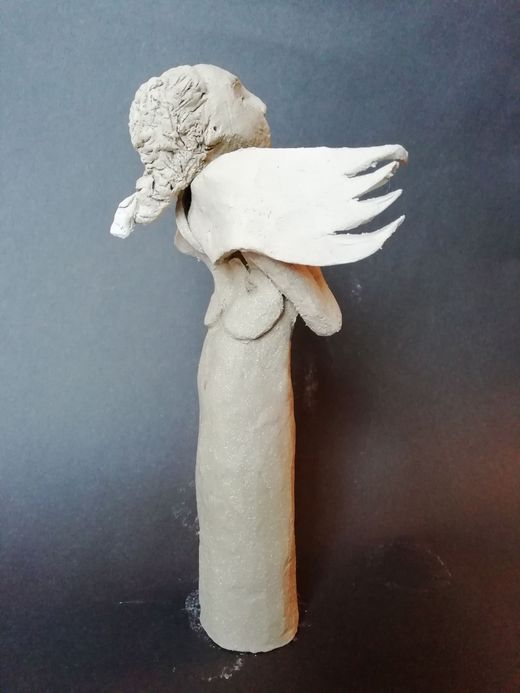 Clay sculpture of an angel with folded wings, looking upward.