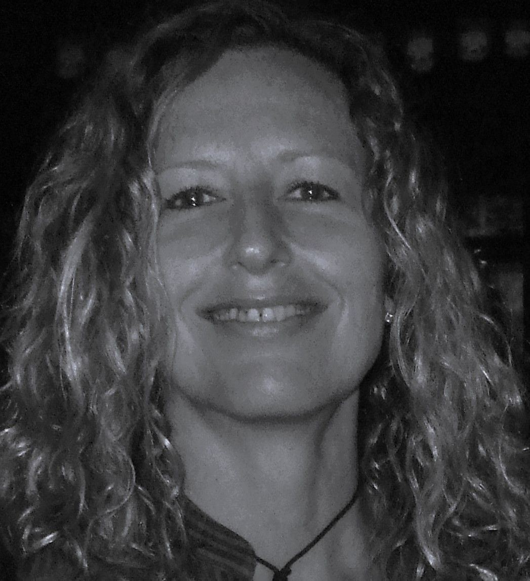 Woman with curly hair smiles, looking toward the camera. Black and white portrait.