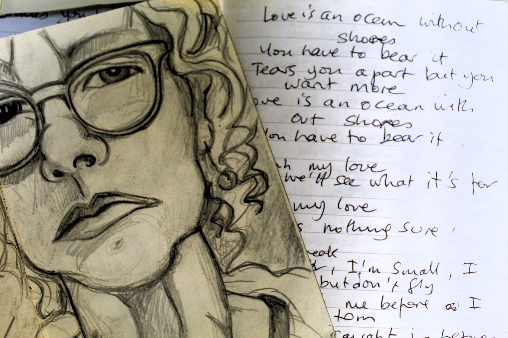 Pencil sketch of a person wearing glasses with handwritten lyrics about love on a page beside them.