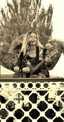 Woman playing guitar on stage, singing with long blonde hair, outdoors.