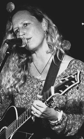 Woman with long hair singing and playing acoustic guitar.