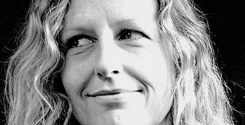 Woman with curly hair smiles, looking to the side. Black and white photo.