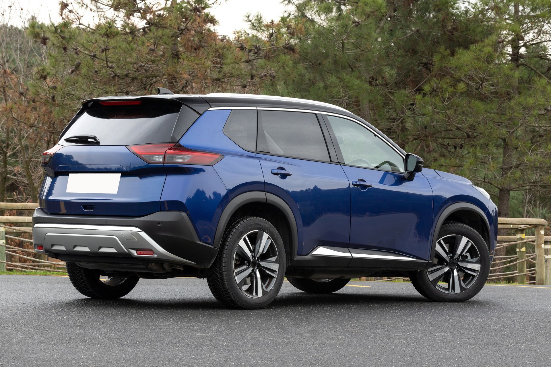 A blue Nissan Rogue SUV parked outdoors on asphalt with trees in the background.